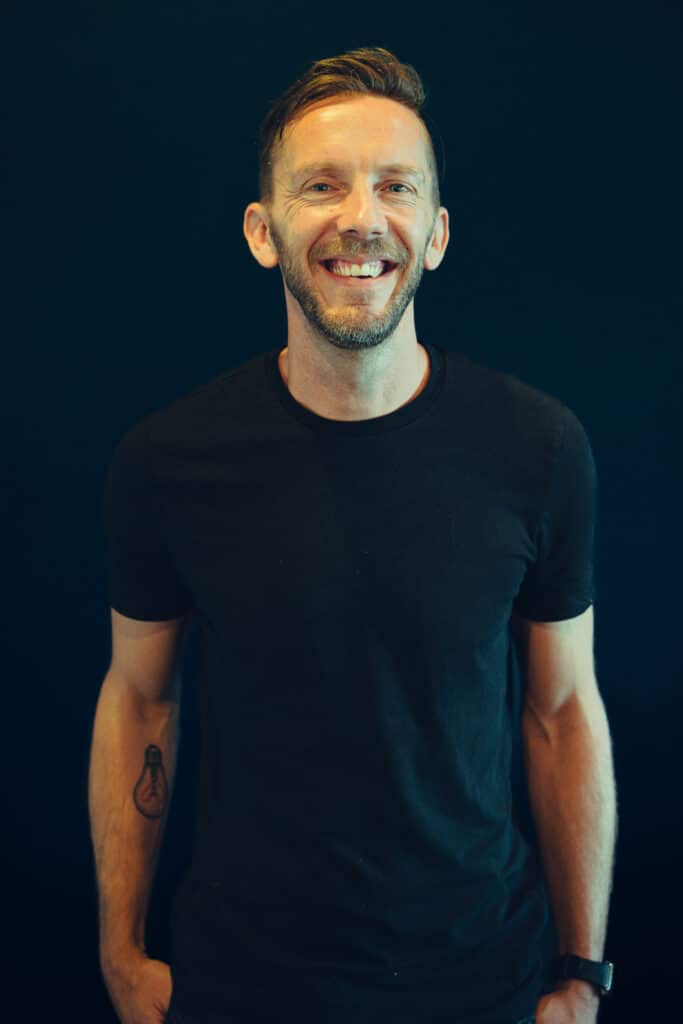 a man in a black t shirt smiles at the camera