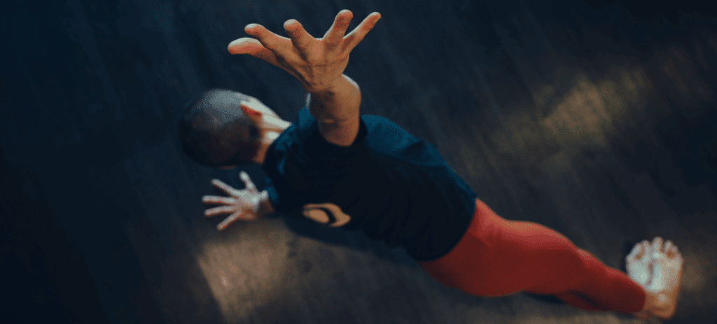 An aerial shot of a woman side planking in a yoga pose with her arm outstretched to the camera