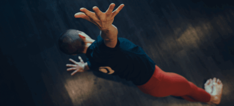 An aerial shot of a woman side planking in a yoga pose with her arm outstretched to the camera