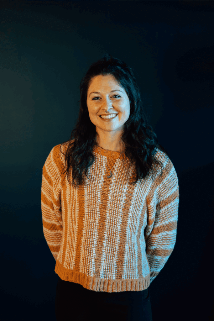 a woman in a striped sweater smiles in front of a dark wall