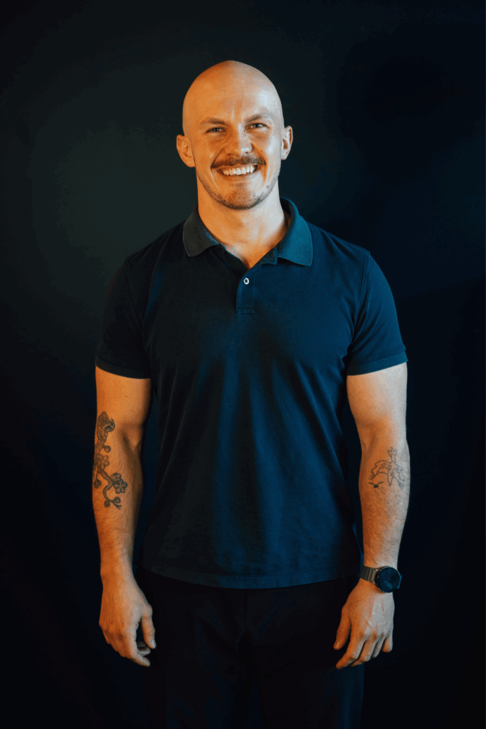 a man in a short sleeved blue polo shirt smiles in front of a dark wall