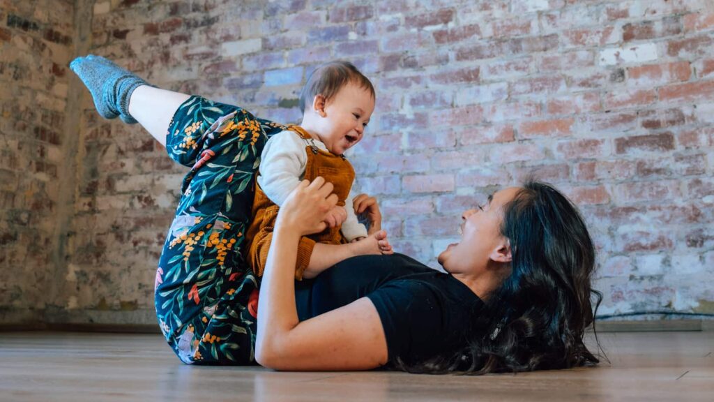 a woman lays in a yoga pose with a smiling baby in her lap