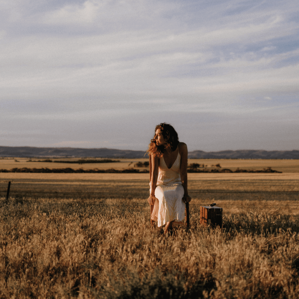 A woman sits on a chair in a sunlit field.
