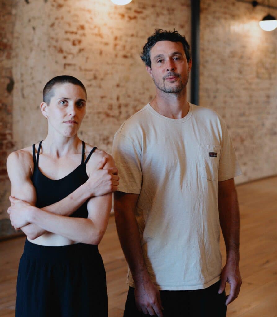A man and a woman stand side by side looking at the camera
