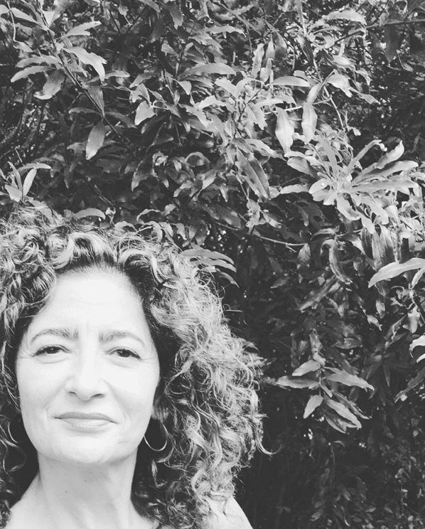 a black and white photo of a woman in front of a large bush or tree