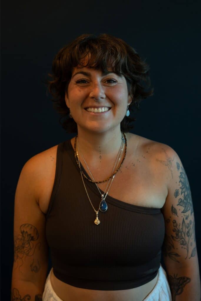 A woman with short brown hair and tattoos smiles at the camera